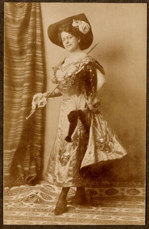 Posando con sombrero de ala alzada, vestido con lazo, y sosteniendo un bastón