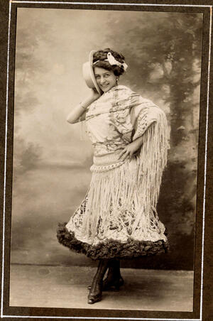 Con vestido corto de lentejuelas y mantón de fleco, sujeta el sombrero contra la mejilla derecha